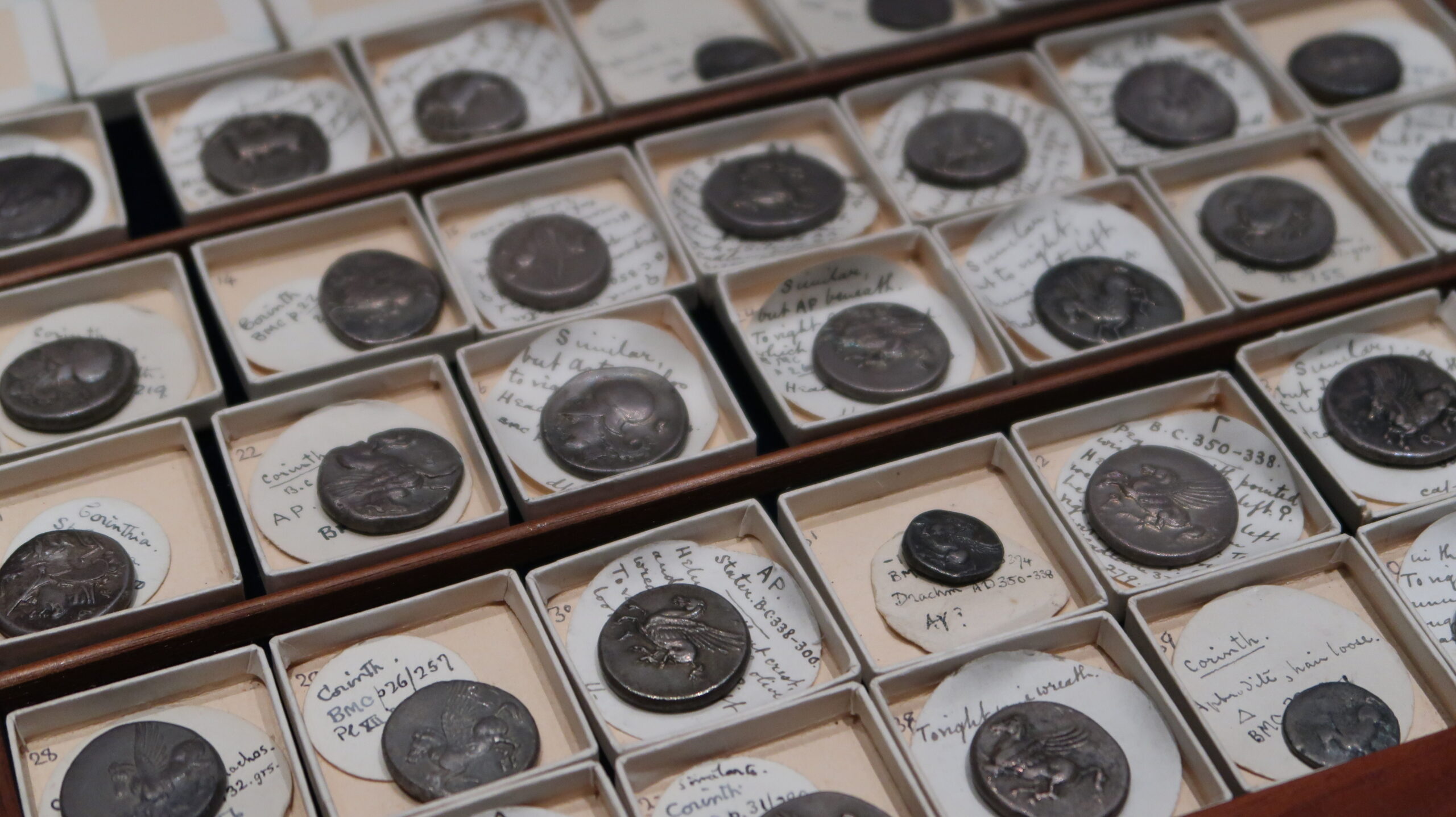 Wooden tray containing 28 silver coins which feature Pegasus the flying horse.