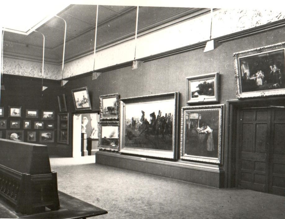 Black and white gallery photograph showing large paintings on a central wall.